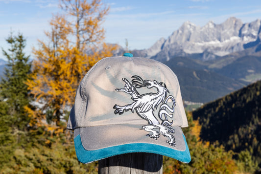 Snapback Basecap - "Steiermark Rockt" mit gesticktem Panther-Wappen, türkis-blauem Schildrand, fotografiert vor alpiner Bergkulisse in der Sonne